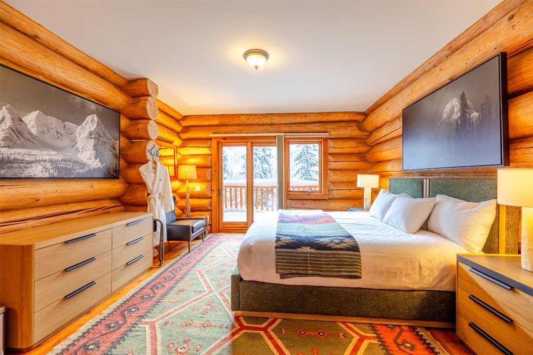 A warm timber guest room in Cedar Lodge, with white bedding and a private balcony overlooking the snowy forest