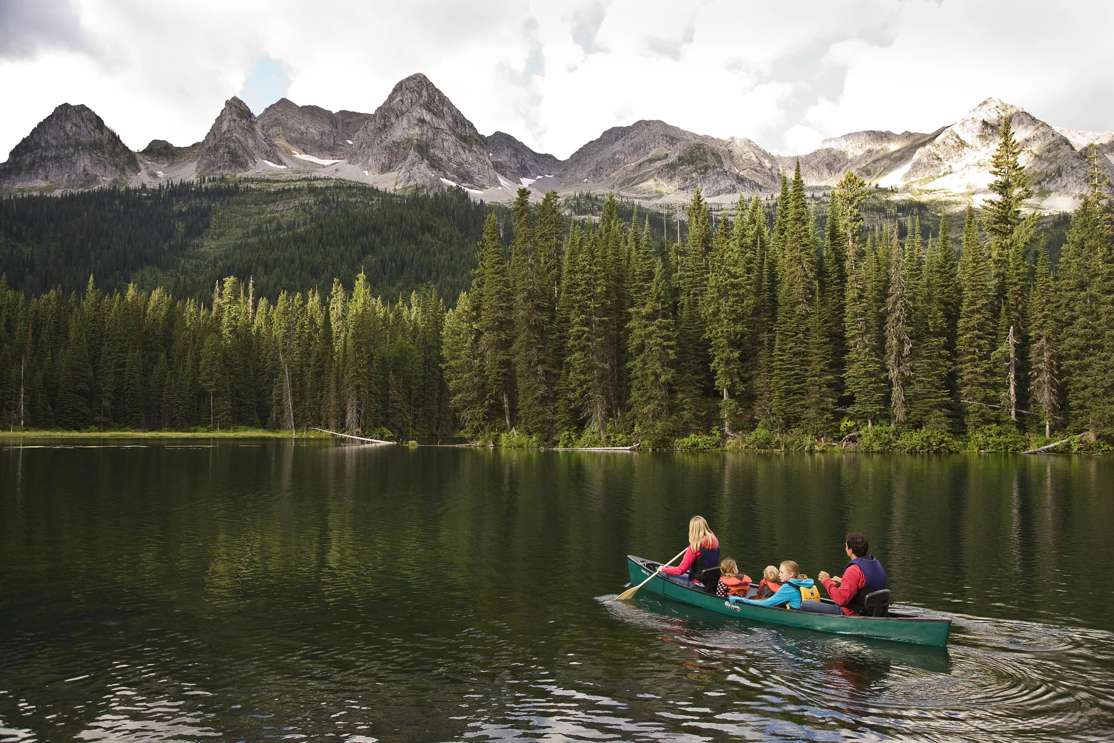 A family paddling a green canoe on Island Lake beneath the Lizard Range