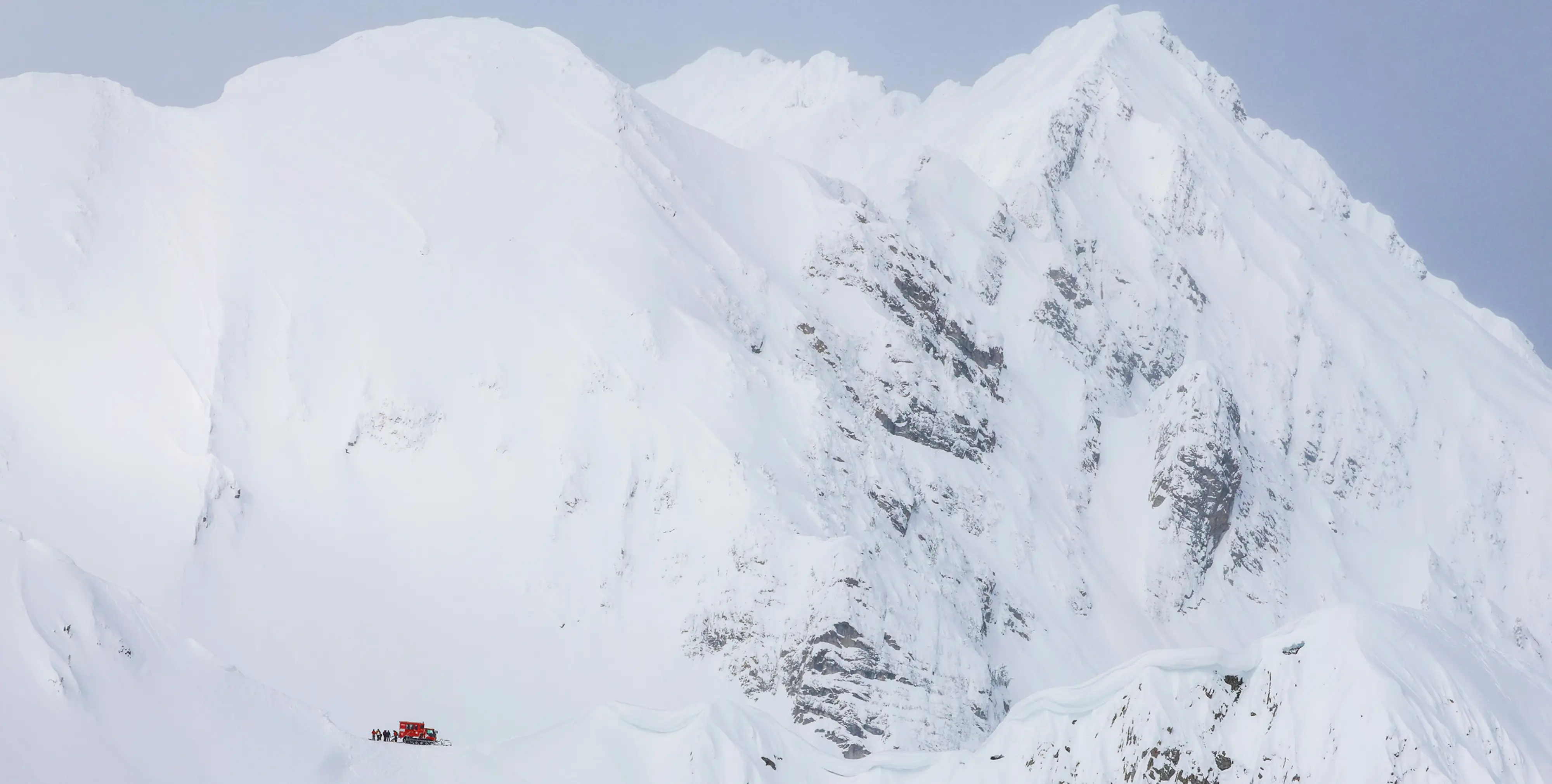 A red snowcat beneath towering snow-covered peaks at Island Lake