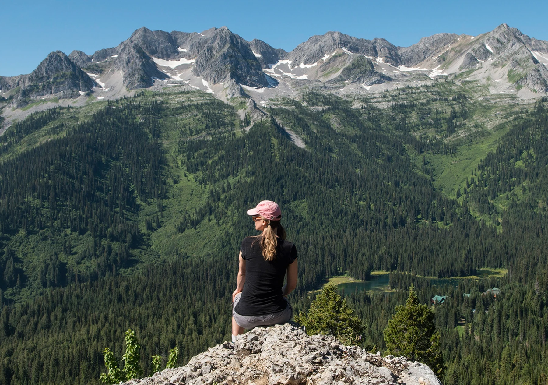 A hiker sitting at Tamarack Viewpoint above Island Lake and the Lizard Range.