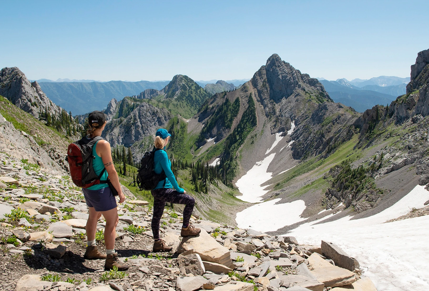 Two hikers at Upper Nonstop Pass on the Goldilocks Trail overlooking an alpine basin.