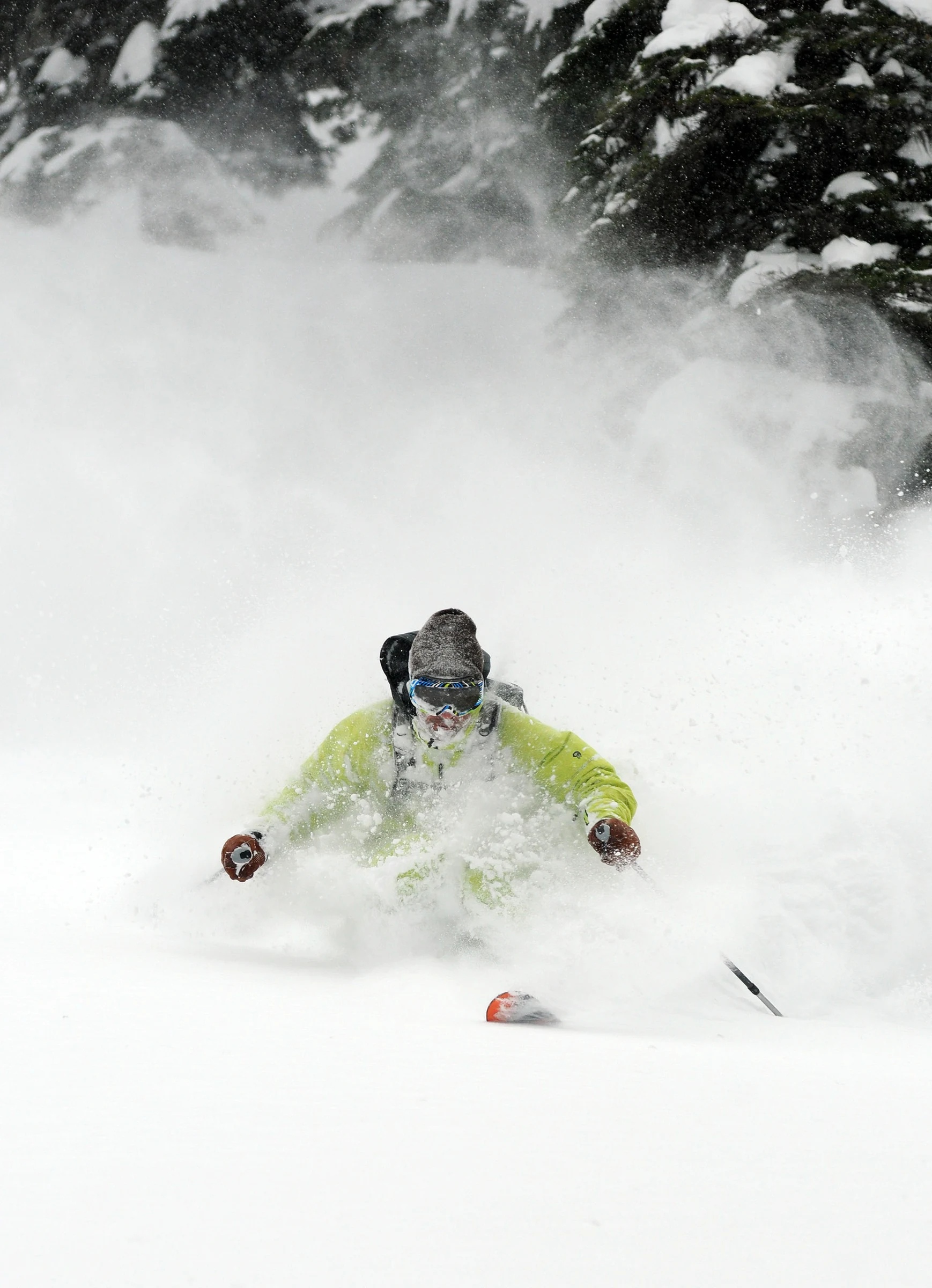 A skier in a lime jacket making a deep powder turn among snowy trees at Island Lake