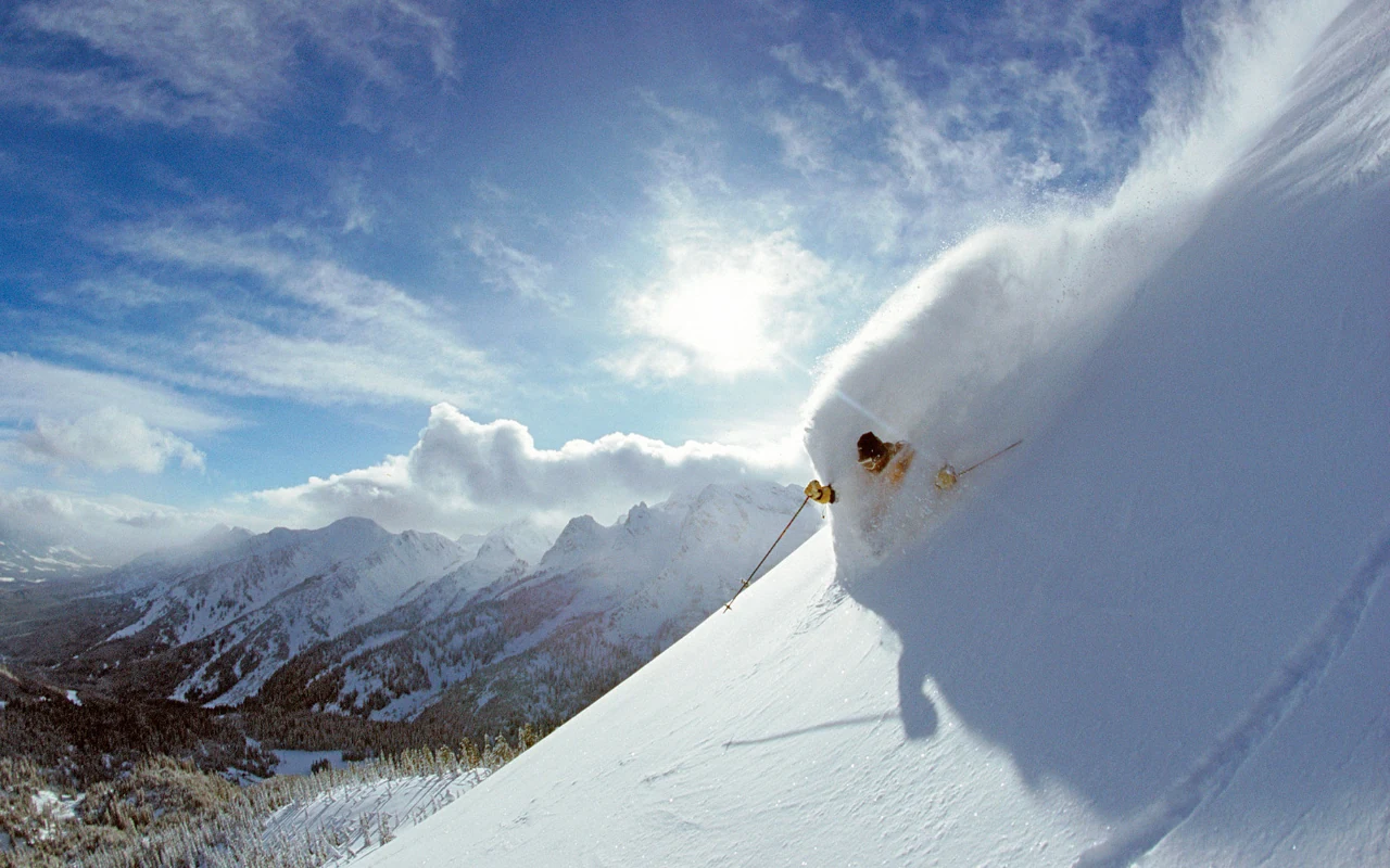 A skier emerging from a sunlit cloud of powder at Island Lake
